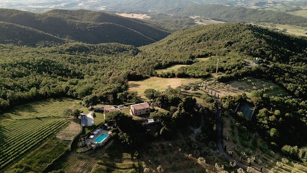 Una vista aerea di una tenuta con piscina, vigneto e edifici immersi tra dolci colline boscose.