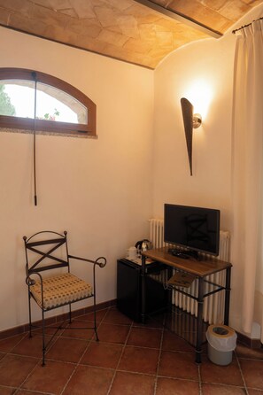 Une petite pièce avec un bureau en bois, une chaise, un téléviseur et un radiateur.