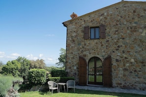 A stone building with a small window and two doors, surrounded by greenery.