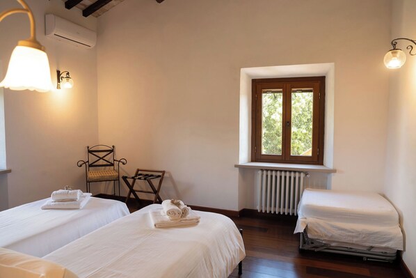 A room with two beds, a radiator, a window with a view, and a chair.