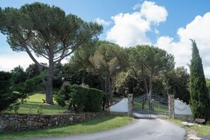 Une entrée fermée par un portail, avec un mur en pierre, un portail en métal et un chemin menant à un bâtiment.
