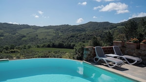 Una piscina con lettini e un muro in pietra, affacciata su un paesaggio montuoso.