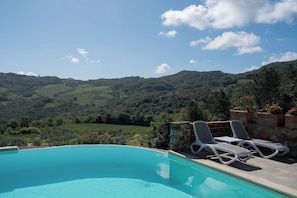A swimming pool with lounge chairs and a stone wall, overlooking a mountainous landscape. - Agriturismo Aia Leccioni (Pomarance)