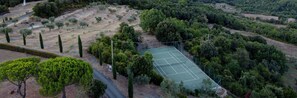 An aerial view of a tennis court surrounded by trees and a hilly landscape.