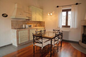 A compact kitchen with a dining area, featuring a stove, microwave, sink, and a window with curtains.