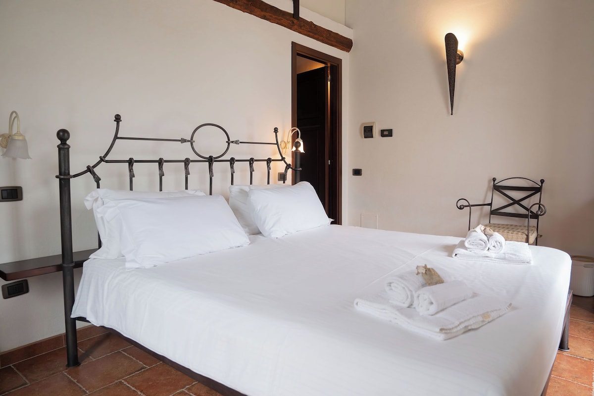 A neatly made bed with white linens, a metal headboard, and a wall-mounted light fixture.