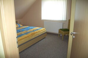 Ein Schlafzimmer mit einem Bett, einem Heizkörper, einem Fenster mit Jalousien und einer Tür.