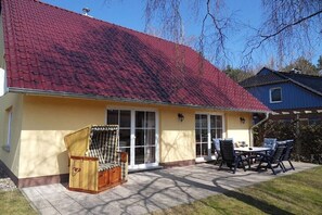 Ein Haus mit rotem Ziegeldach, einer überdachten Terrasse mit Gartenmöbeln und einer gelben Außenwand.