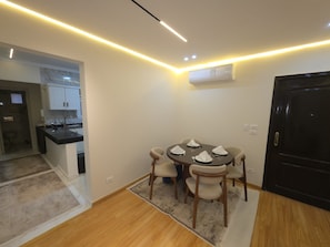 A dining area with a round table, chairs, and a rug. There is a kitchen visible in the background. - Luxury stay in Sheikh Zayed, beside schools, malls (6th October)