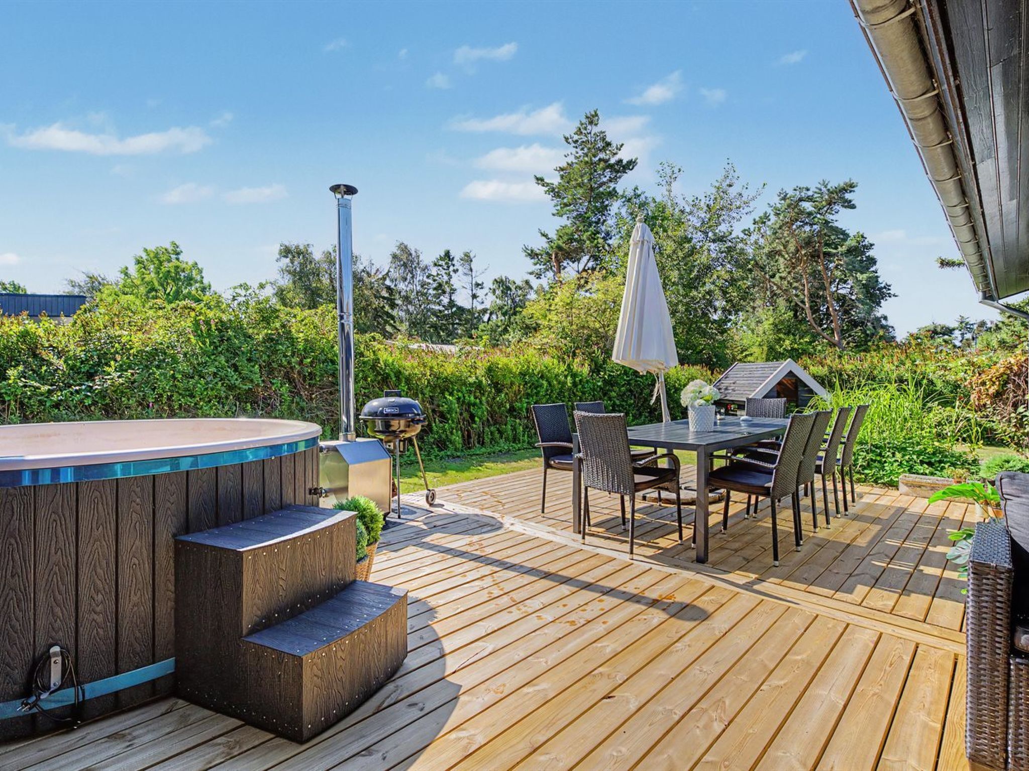 A wooden deck with a hot tub, outdoor seating, and a barbecue grill.