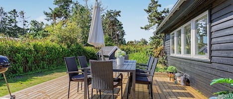An outdoor patio with a table and chairs, surrounded by greenery and a wooden deck.