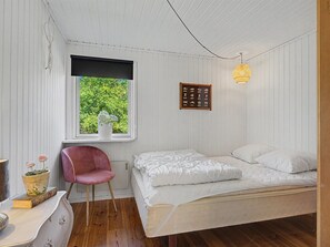 Ein Schlafzimmer mit einem Einzelbett, einem Sessel, einem Fenster mit Blick ins Grüne und einer Wandleuchte.