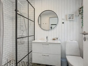 Un bagno con cabina doccia in vetro, uno specchio rotondo, un lavandino bianco e un water.