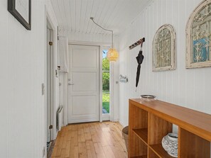 Ein Flur mit Holzboden, weißen Wänden, einer weißen Tür und einem Holztischchen mit einer Schale darauf.
