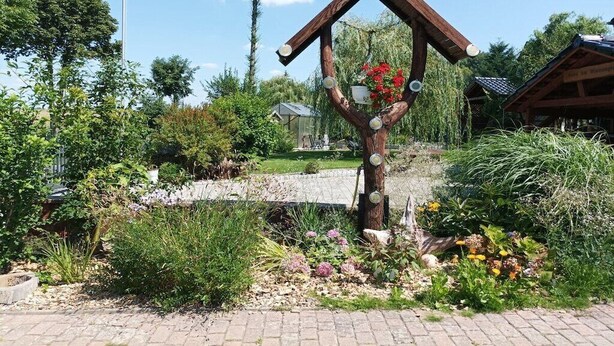 Een tuin met een houten constructie, een vlag en een klein gebouw op de achtergrond.