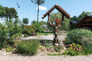 A garden with a wooden structure, a flag, and a small building in the background.