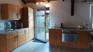Een compacte keuken met houten kastjes, een inbouwoven en een schuifdeur naar een buitenruimte.