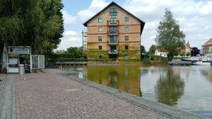 Een gebouw van baksteen met een balkon, een geplaveid pad en een waterpartij op de voorgrond.