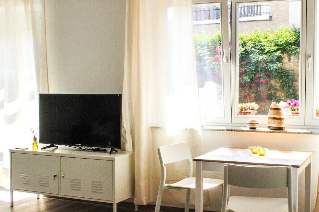 Ein Zimmer mit Fernseher auf einem Schrank, einem Tisch mit Stühlen und einem Fenster mit Blick auf Grünflächen.