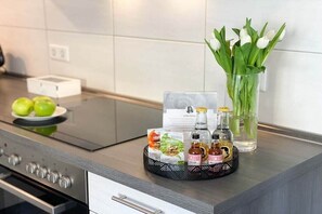 Eine Küchenarbeitsplatte mit einer Serviertablett voller Gewürze, einer Vase mit weißen Blumen und einem Teller grüner Äpfel.