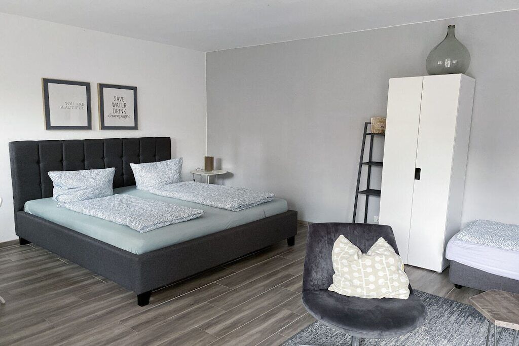 A modern bedroom with a bed, a chair, a wardrobe, and two framed motivational quotes on the wall.
