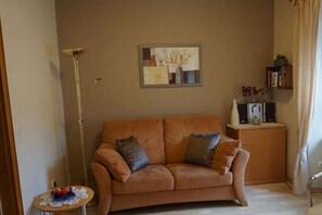 A living room with a sofa, a floor lamp, a small table with fruit, and a painting on the wall. - Holiday apartment with 1 bedroom (Enkirch)