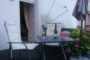A balcony with a table, two chairs, a bottle of wine, and a flower pot. - Holiday apartment with 1 bedroom (Enkirch)
