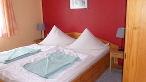 A single bed with white bedding and two pillows, a bedside table with a lamp, and a red wall. - in the holiday village "Boeker Mühle" (Boeker Mühle)