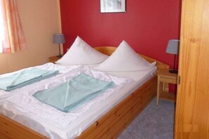 A single bed with white bedding and two pillows, a bedside table with a lamp, and a red wall. - in the holiday village "Boeker Mühle" (Boeker Mühle)