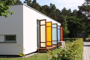 Ein modernes Gebäude mit weißer Fassade, einem kleinen Fenster und farbenfrohen Schiebetüren.