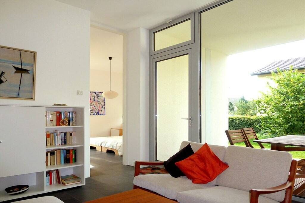 A modern living room with a sofa, a bookshelf, and a large window.