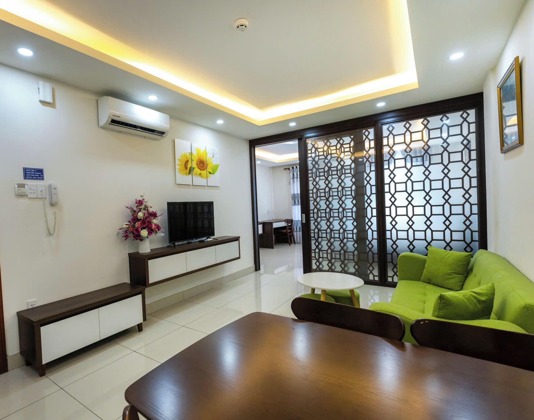A modern living room with a wooden coffee table, a green sofa, a TV on a white cabinet, and a decorative wall panel.