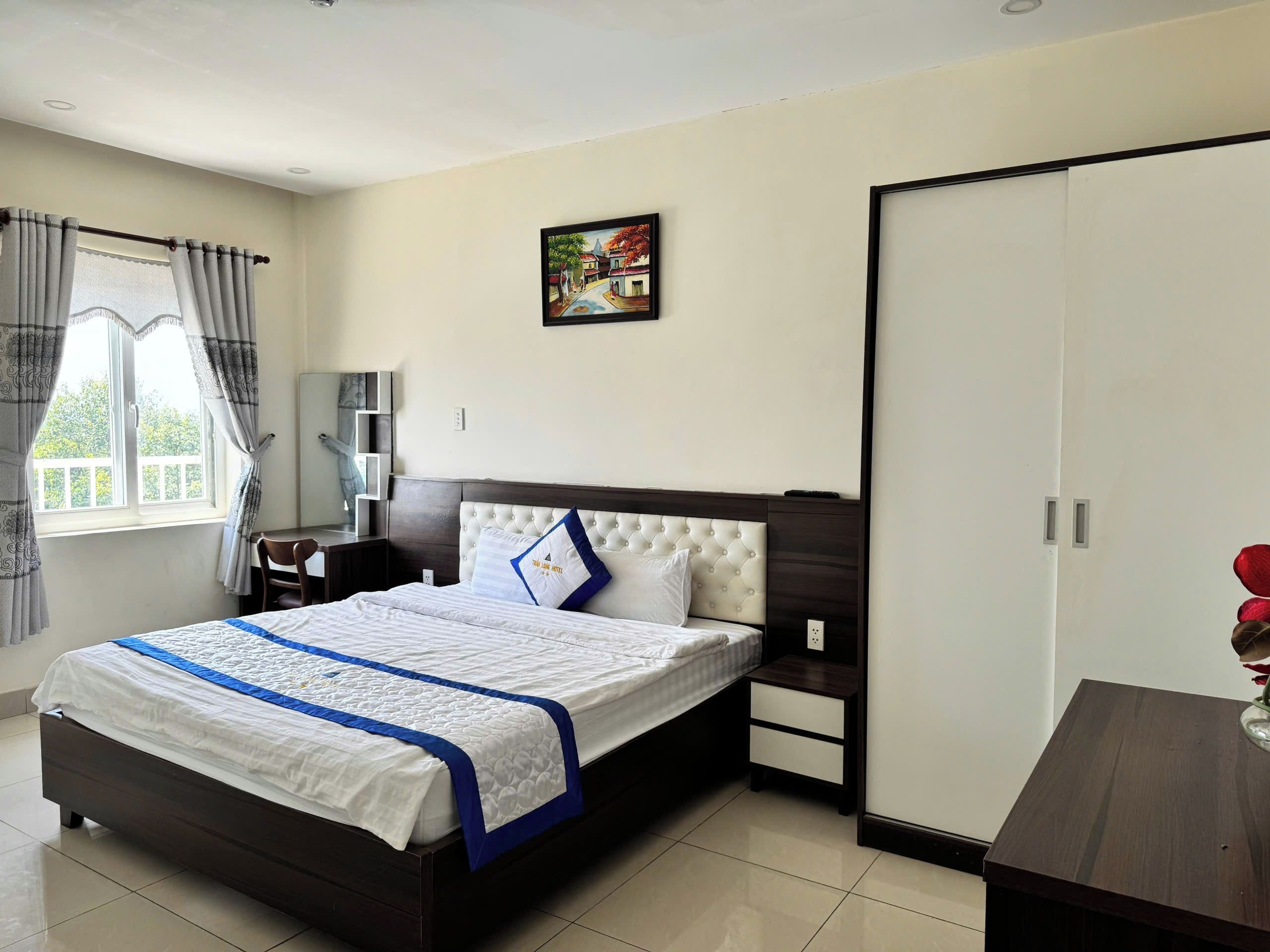 Habitación de hotel con cama, mesitas de noche, armario, un cuadro en la pared y ventana con cortinas.