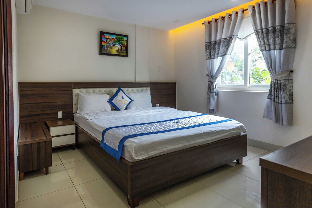 Un dormitorio ordenado con cama, mesita de noche y ventana con cortinas.