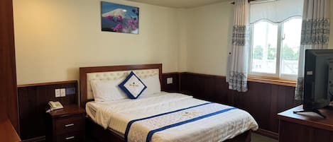 A hotel room with a bed, bedside table, TV, and a window with curtains.