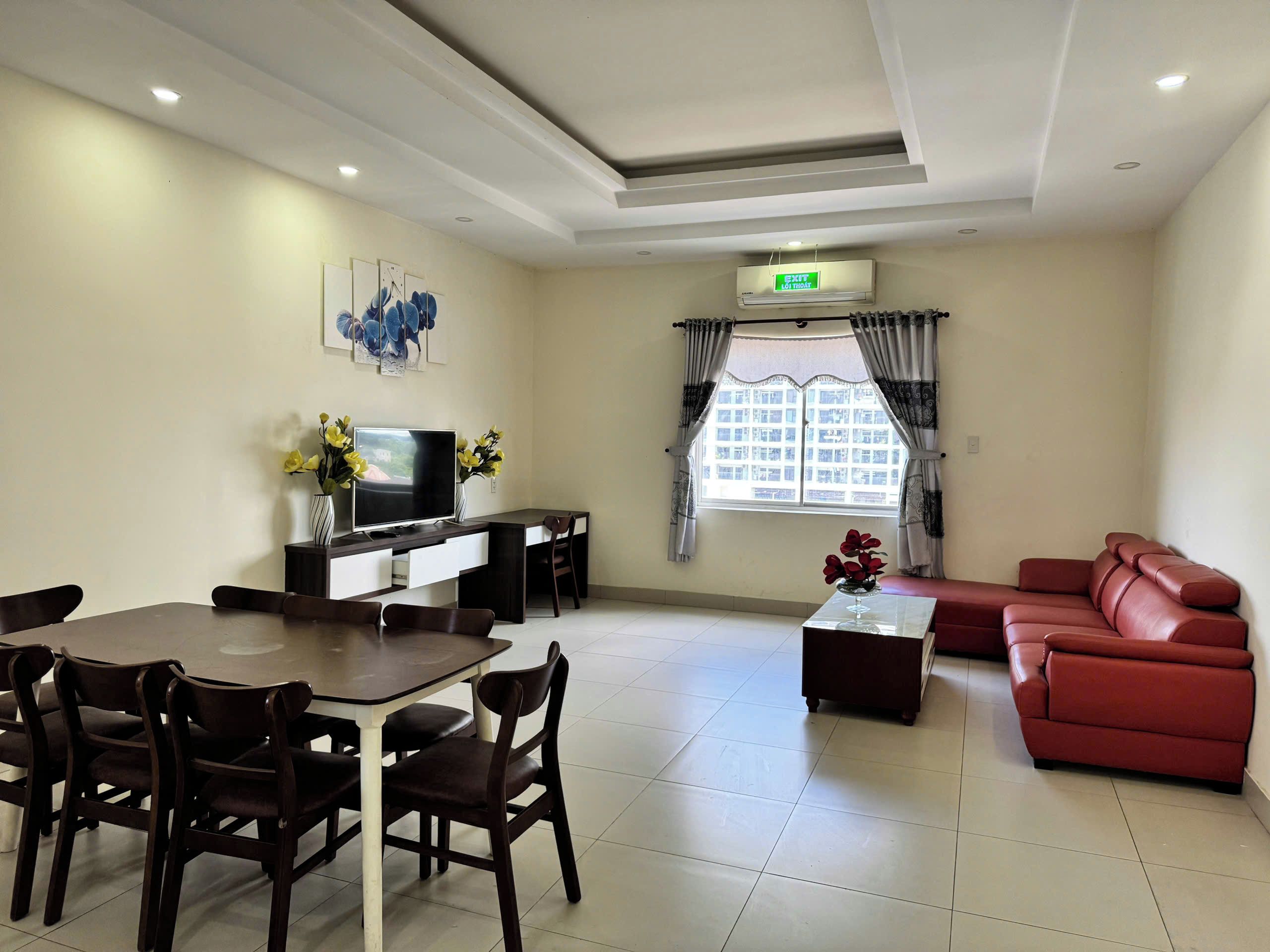 Habitación de hotel con una mesa de comedor, sillas, sofá, televisor y ventana con cortinas.
