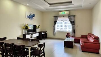 Habitación de hotel con una mesa de comedor, sillas, sofá, televisor y ventana con cortinas.