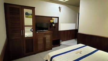 A hotel room with a bed, a wardrobe, a television, and a small shelf with flowers.