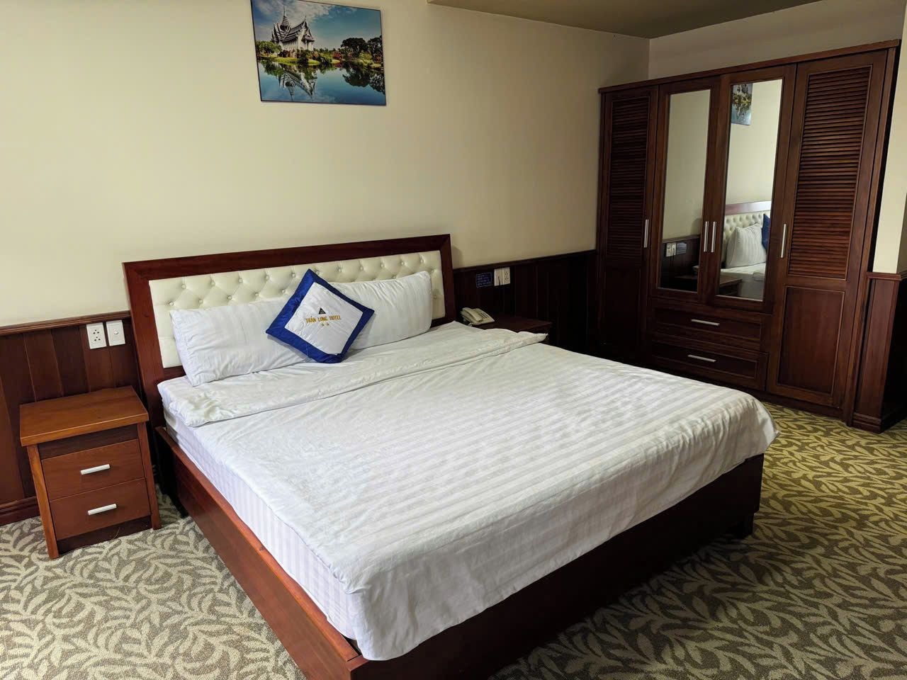 A hotel room with a bed, a nightstand, a wardrobe, and a painting on the wall.