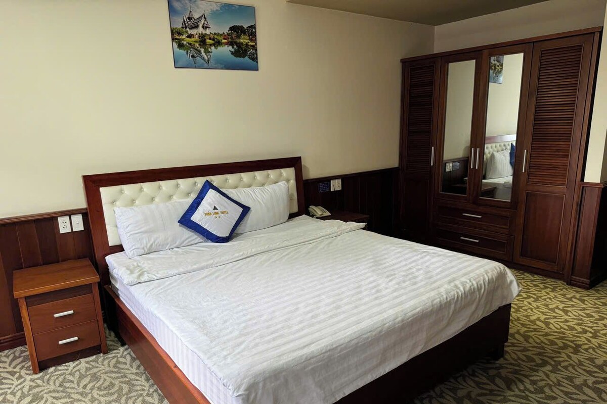 Una habitación de hotel con cama, mesita de noche, armario y un cuadro en la pared.