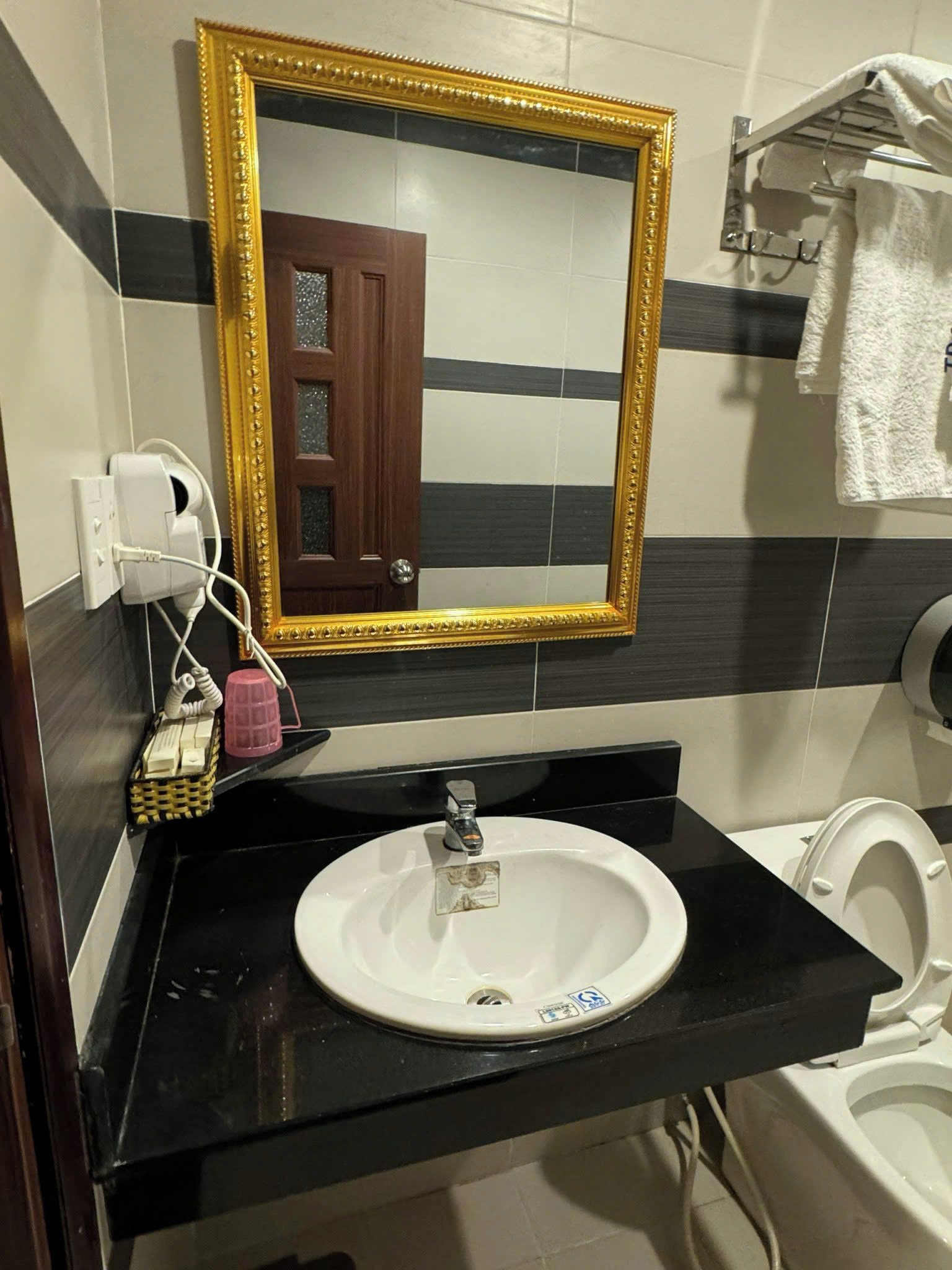 A bathroom with a white sink, a gold-framed mirror, a towel rack, and a toilet.