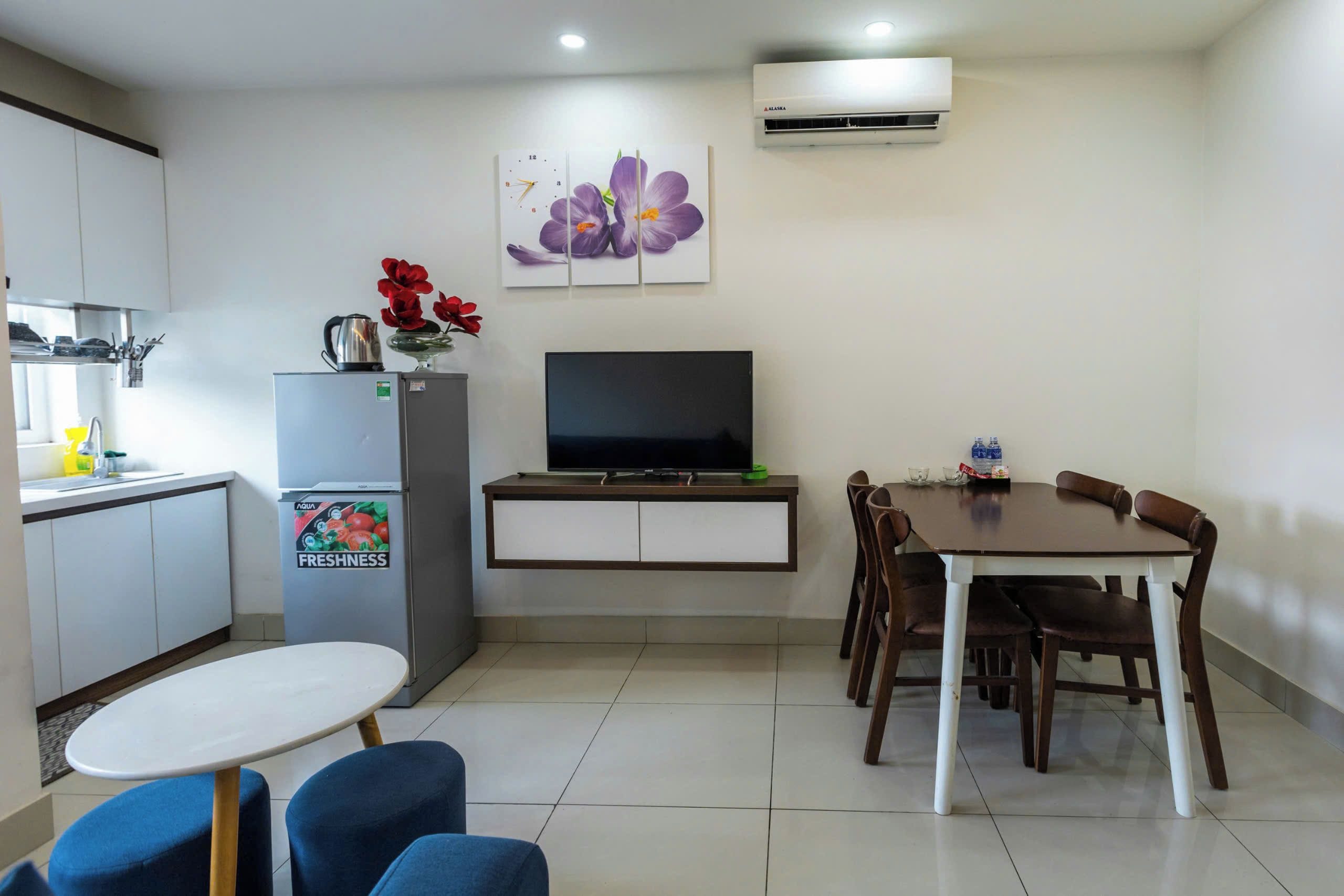 A compact living space with a kitchenette, a dining area with a table and chairs, a flat-screen TV, and a refrigerator.