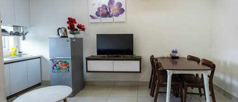 A compact living space with a kitchenette, a dining area with a table and chairs, a flat-screen TV, and a refrigerator.