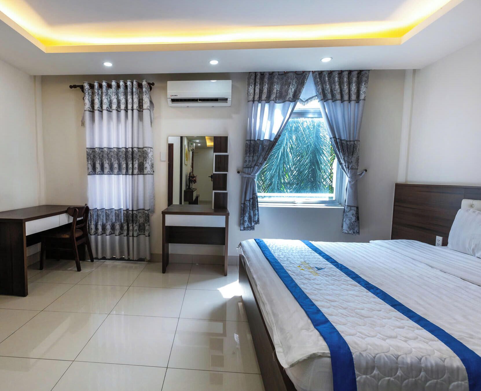 A bedroom with a bed, a desk, a chair, an air conditioning unit, and a window with curtains.