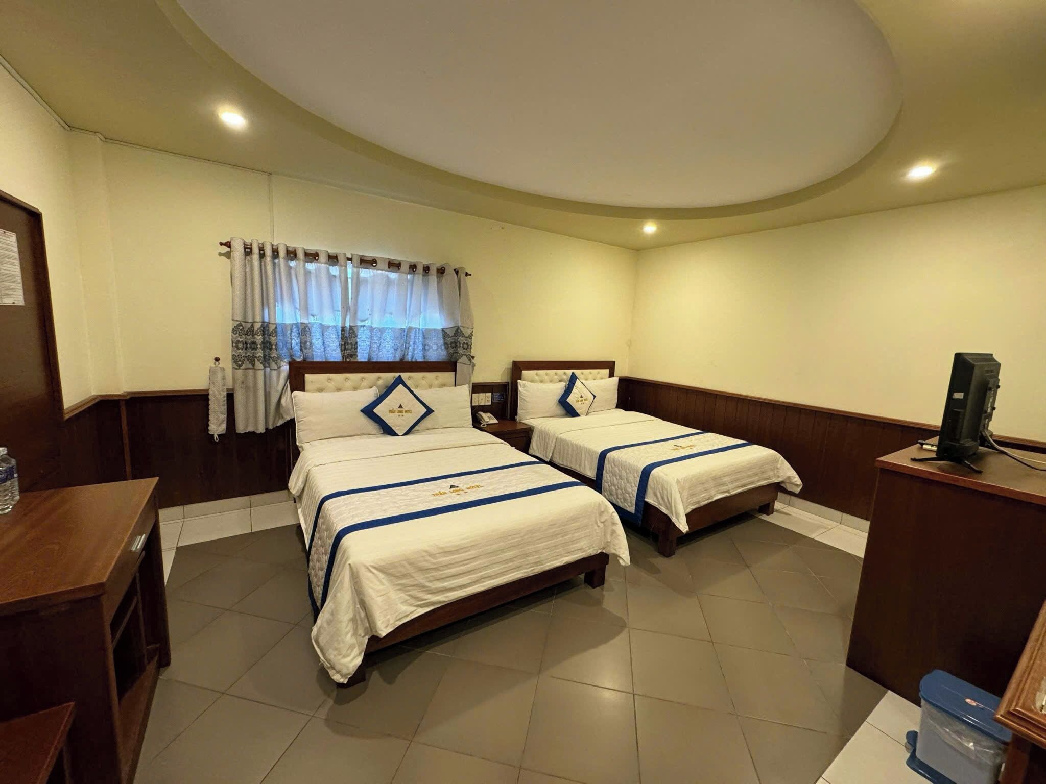 A hotel room with two beds, a desk, a television, and a trash bin.