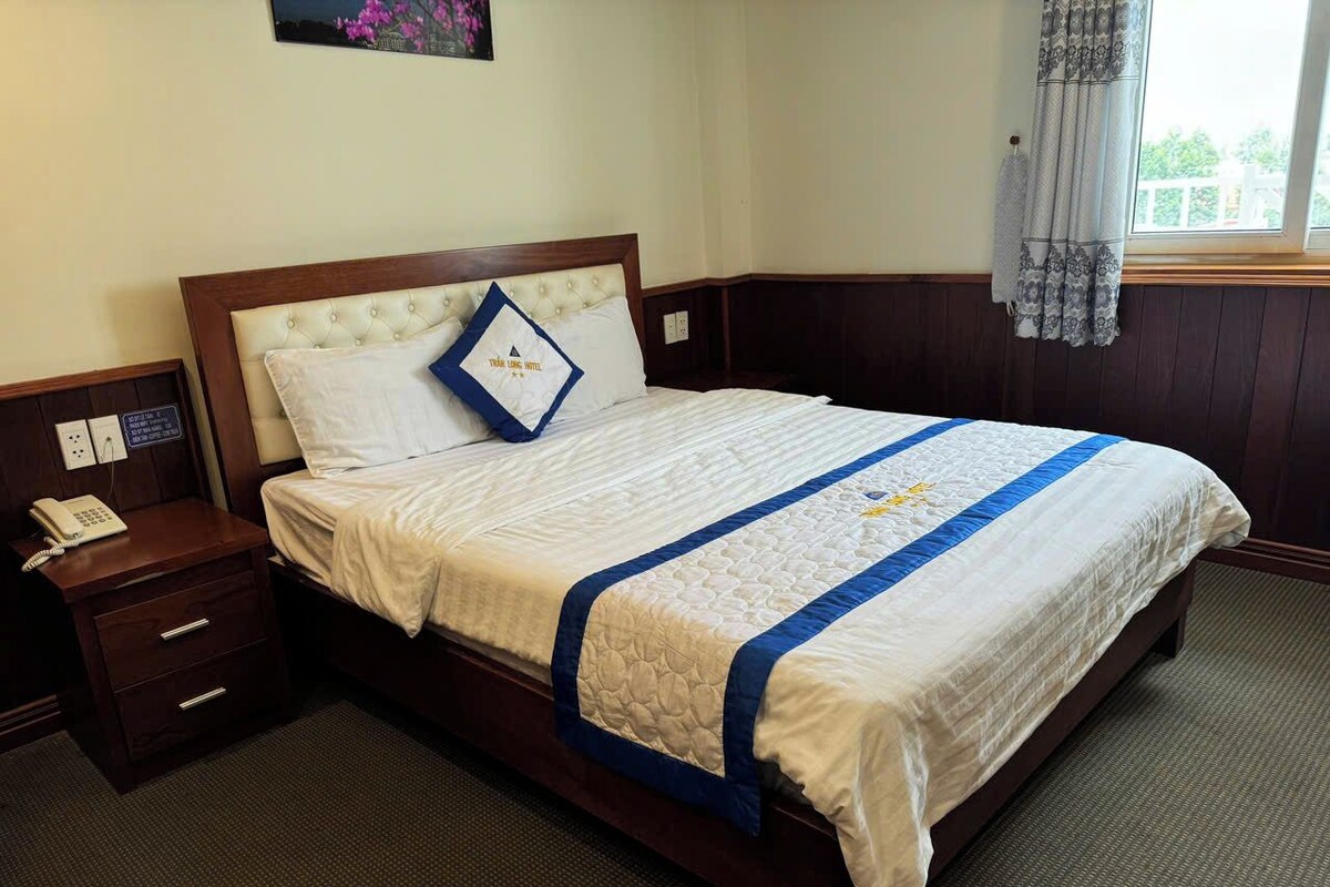 Una habitación de hotel con una cama, una mesita de noche con teléfono y una ventana con cortinas.