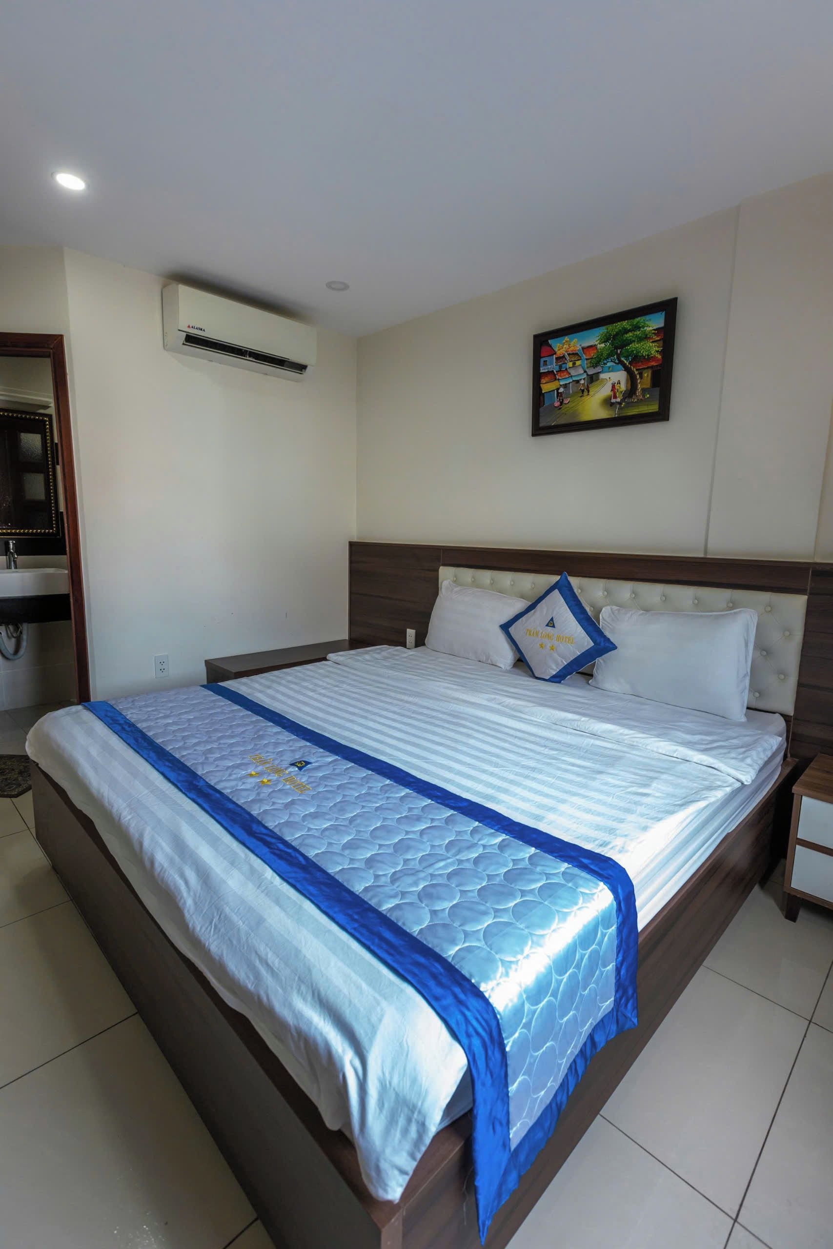 A hotel room with a bed, a nightstand, an air conditioning unit, a wall-mounted TV, and a bathroom with a mirror and sink.
