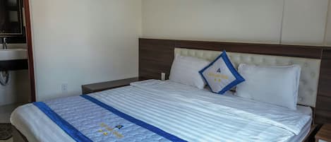Quarto de hotel com cama, mesa de cabeceira, ar condicionado, TV na parede e banheiro com espelho e pia.