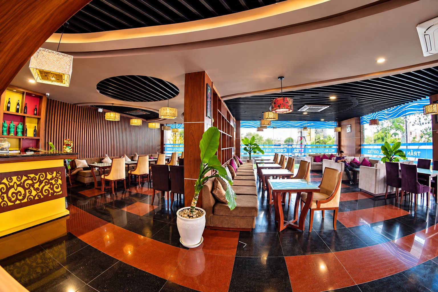 Un moderno vestíbulo de hotel con zona de bar, espacios de descanso y una gran planta en maceta.