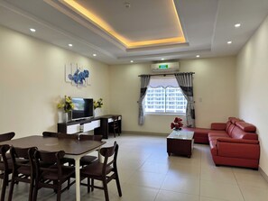 A modern living room with a dining area, a sofa, a TV, and a window with curtains. - Tran Long Hotel (Binh Duong)